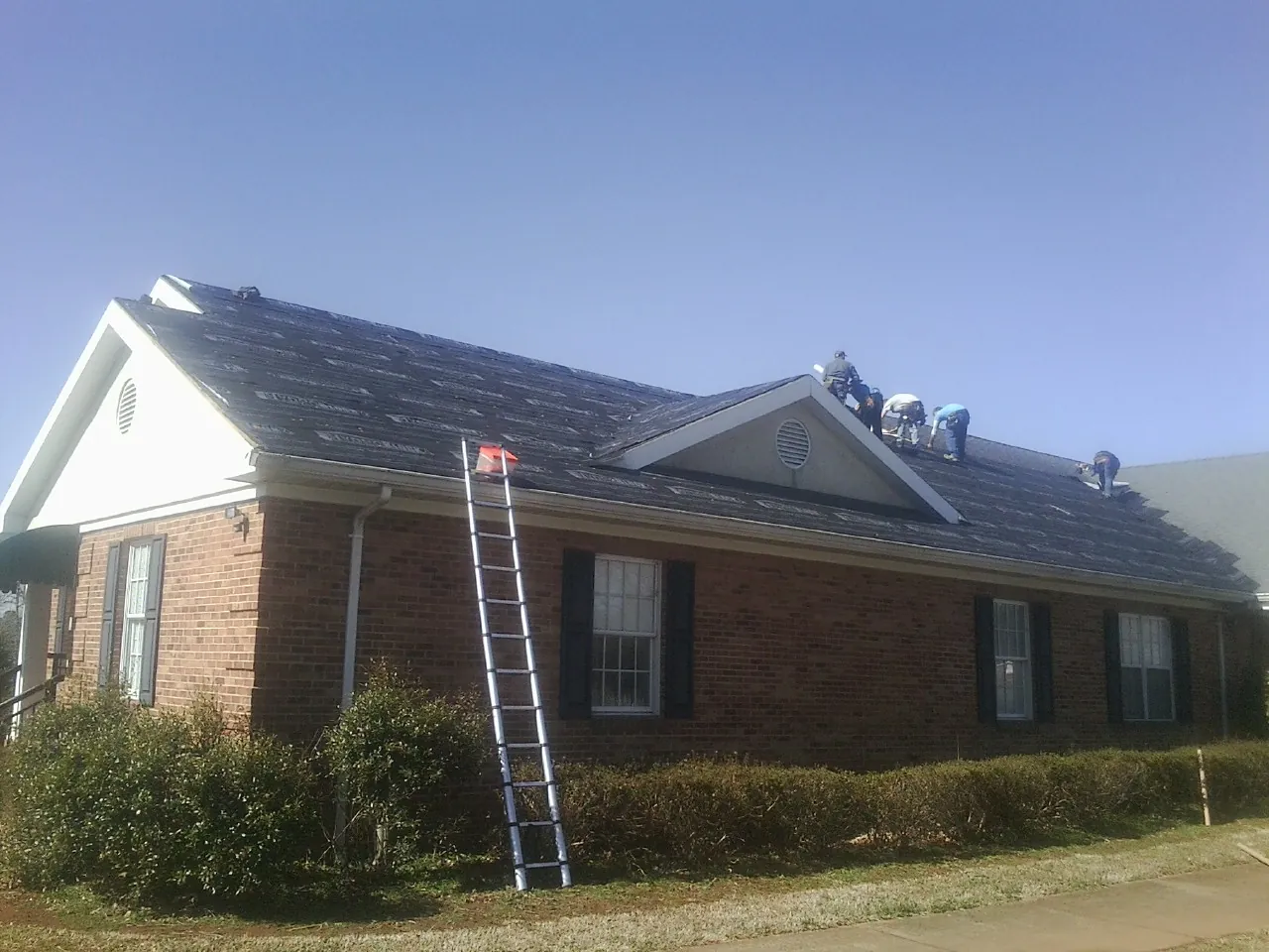 Crew tearing shingles off a brick ranch roof with a ladder set — Emergency Roof Repair work by our crew in Hegins
