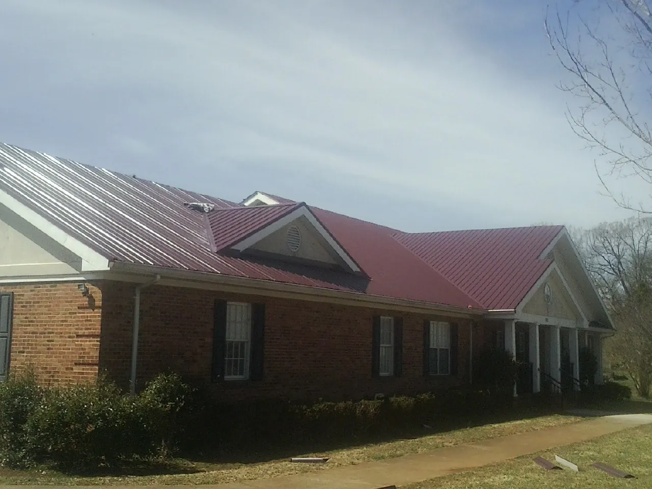 Red metal roof with gabled entries on a long brick building, from a Hail Damage Roof Repair job in Hegins