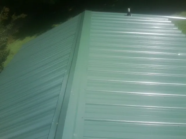 New green metal panels meeting at the ridge of a roof — Flat Roof Repair work by our crew in Hegins