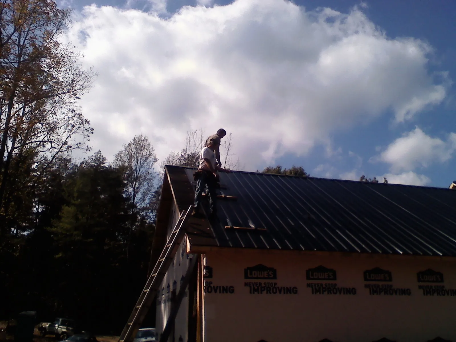 Roofer fastening dark metal panels high against a cloudy sky, from a Roof Inspection job in Hegins