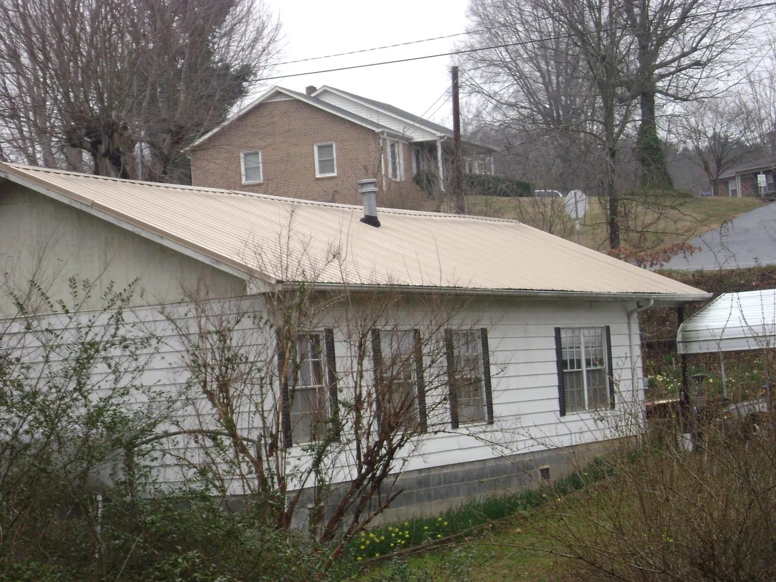 Tan metal roof on a white sided house set into a hillside — Commercial Roofing by Roofing Brothers in Hegins